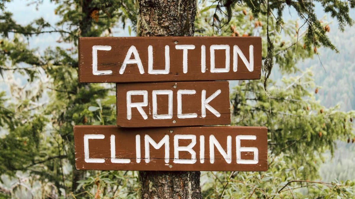 Wooden warning sign on a tree cautioning about rock climbing, set in a forest.