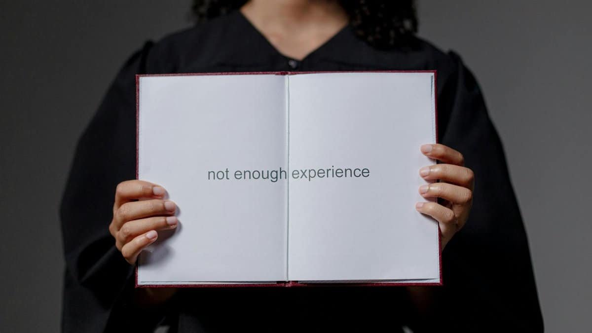 A graduate in cap and gown displays a diploma reading 'not enough experience', highlighting job market challenges.