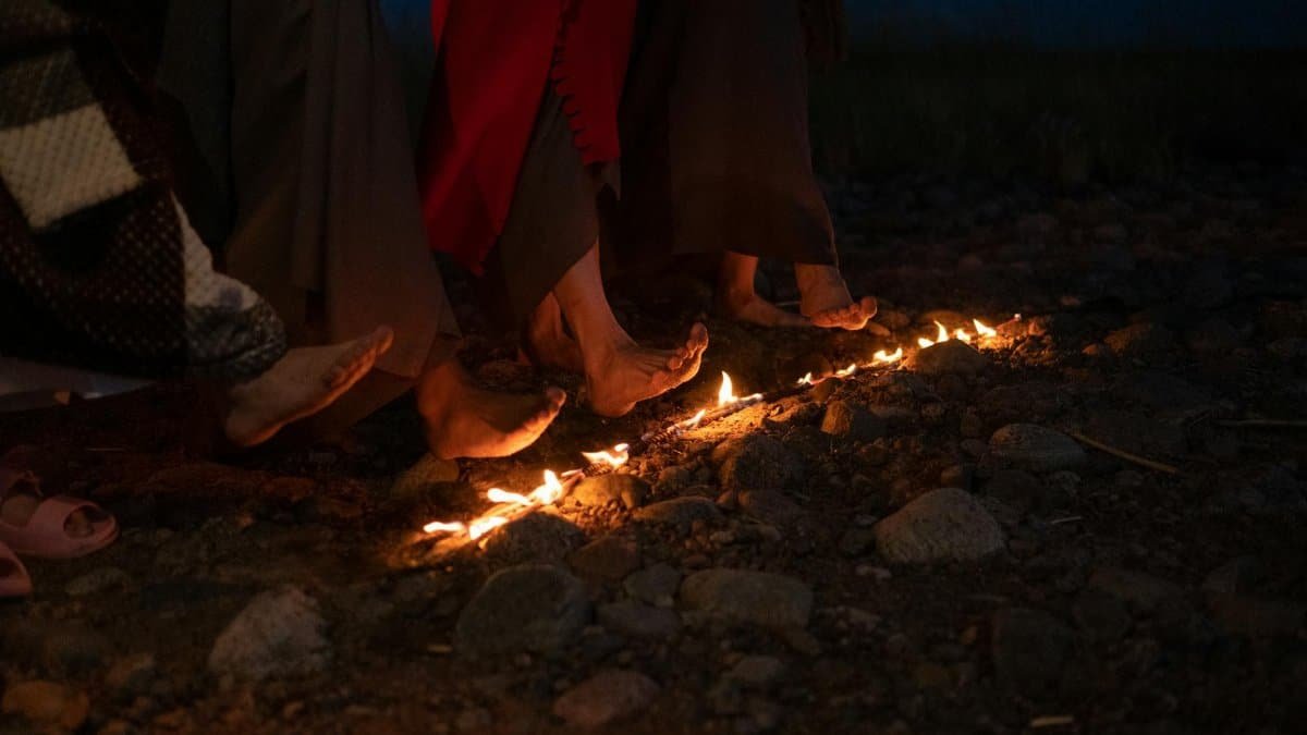 A group of barefoot individuals participating in a firewalking ceremony on a rocky surface at night.