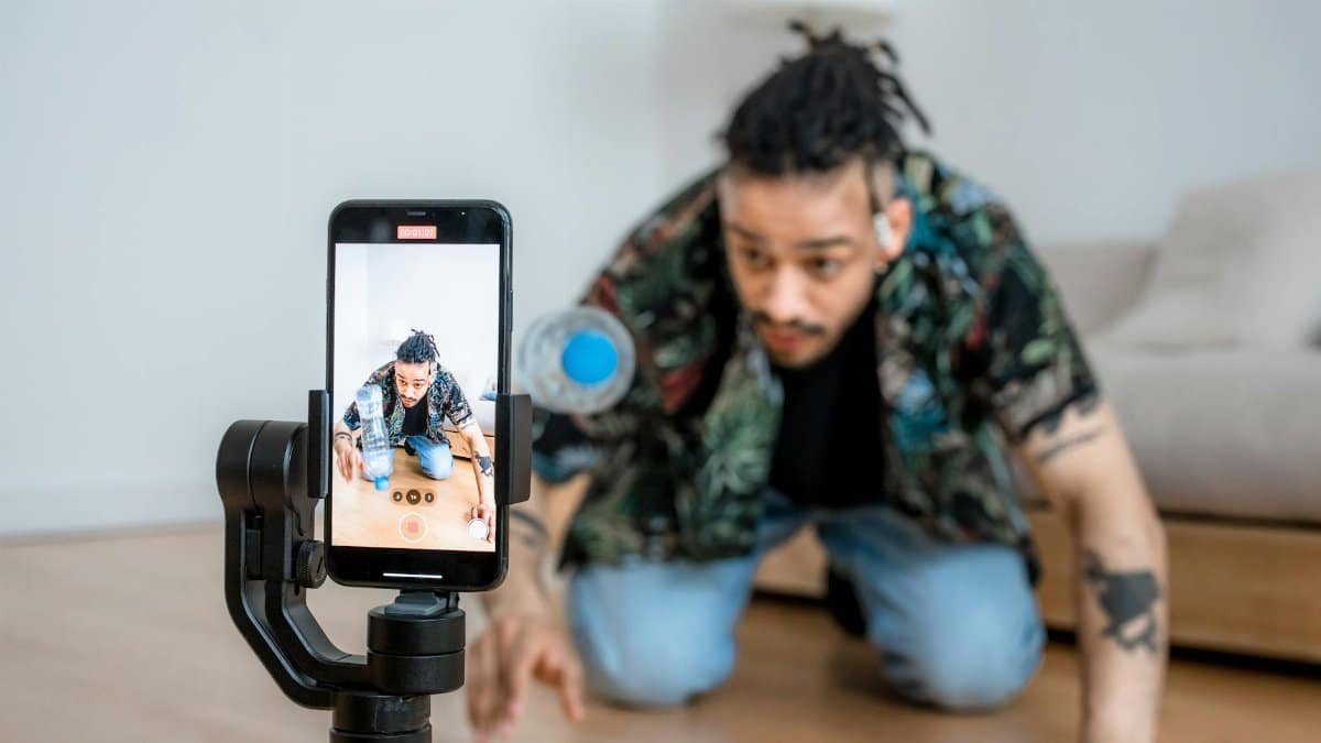 Man filming creative content with smartphone on gimbal indoors.