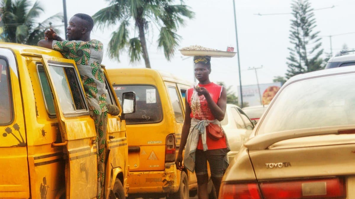 A street vendor balances goods on head while navigating traffic in Lagos, Nigeria.