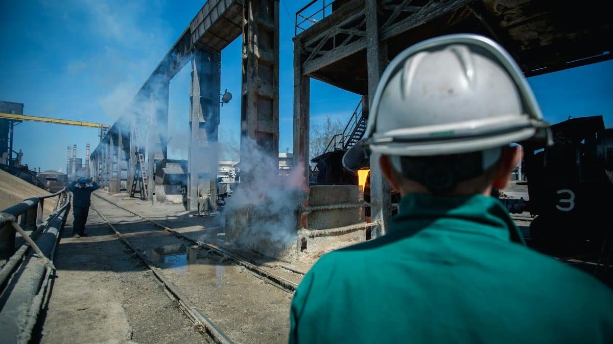 Industrial worker wearing hard hat observing work site with smoke and machinery in a factory setting.