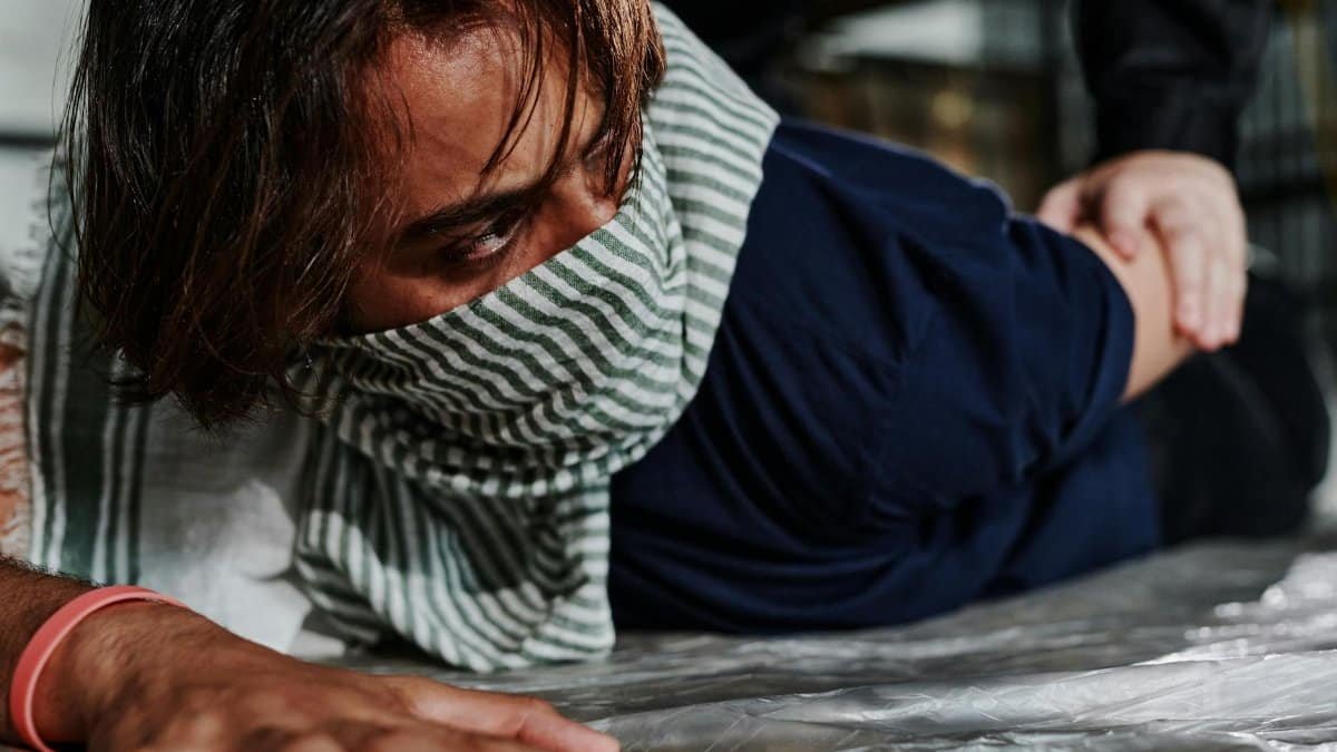 Close-up of a man on the ground wearing a scarf, being restrained by another person.