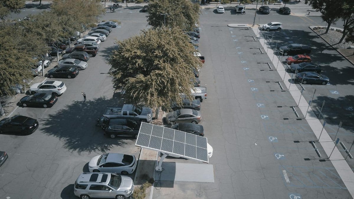 Aerial view of a solar panel charging station in a busy parking lot surrounded by cars and trees.
