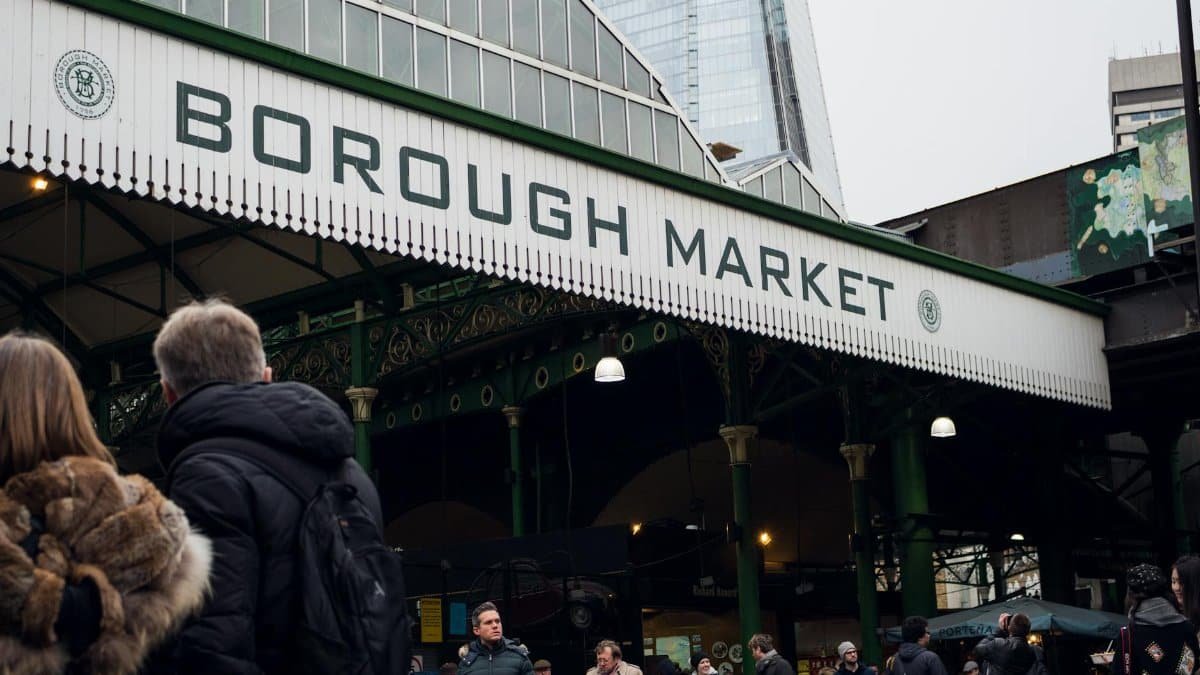 People enjoying a bustling day at London's iconic Borough Market with city skyscrapers in the background.