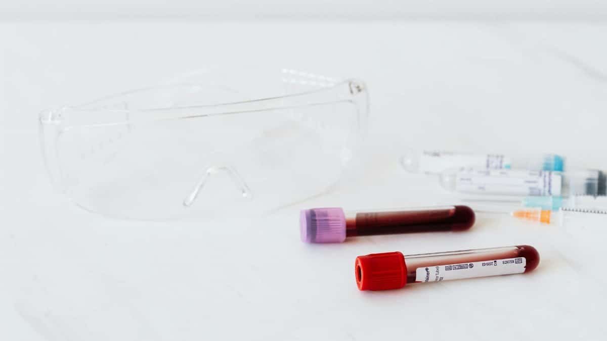 Close-up of medical vials with blood samples and protective eyewear on white background.
