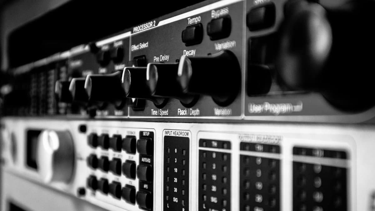 Detailed black and white close-up of an audio mixer highlighting various control knobs and switches.