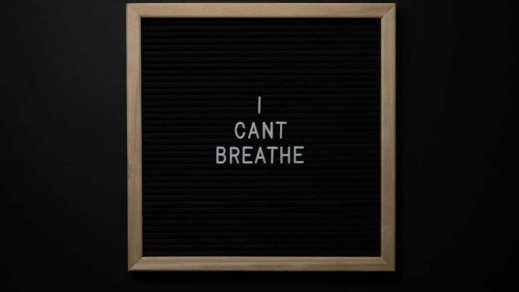 Top view of phrase I Cant Breath on small black signboard with light beige thin frame on black background