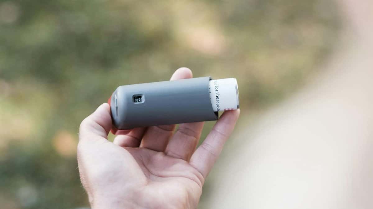 Close-up of a hand holding a grey inhaler in a natural outdoor setting.