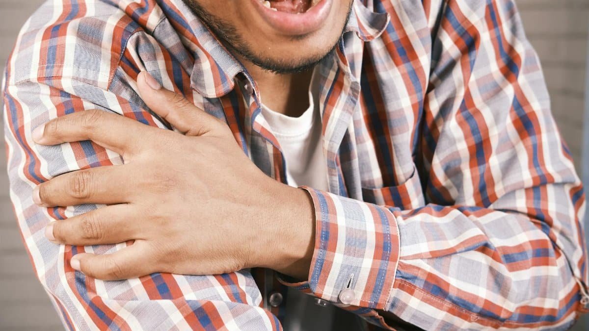 Close-up of a man in plaid shirt experiencing shoulder pain, grasping his arm.