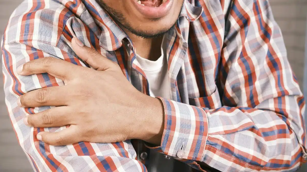 Close-up of a man in plaid shirt experiencing shoulder pain, grasping his arm.