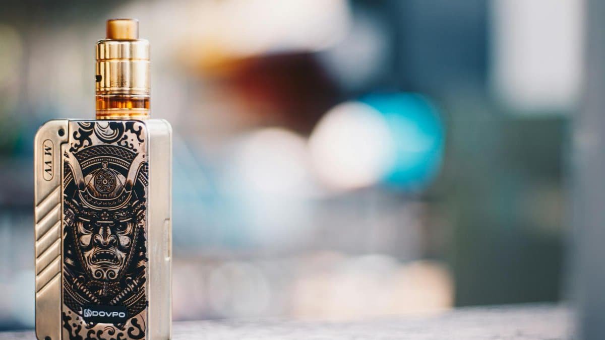 Close-up of a vape device with samurai design, set against a blurred background in Bangkok.