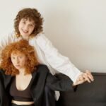 A joyful same-sex couple holding hands on a black leather couch.
