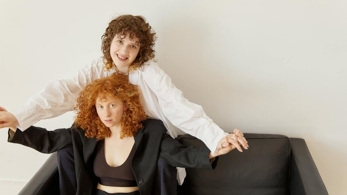 A joyful same-sex couple holding hands on a black leather couch.