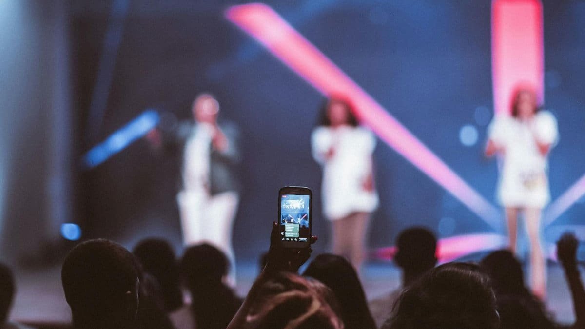 Audience members capture a live music performance on their phones, experiencing vibrant stage lights.