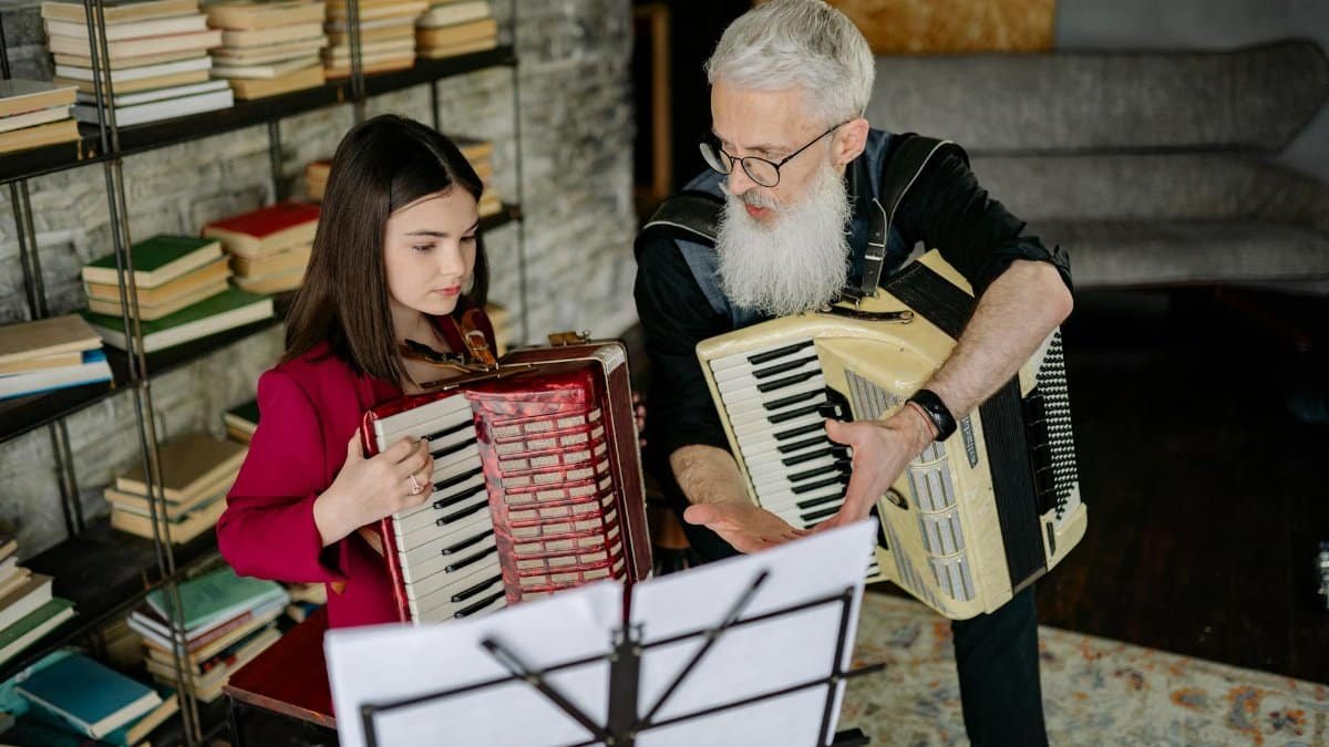 Young girl receiving accordion lessons from an elderly man in a cozy home setting.