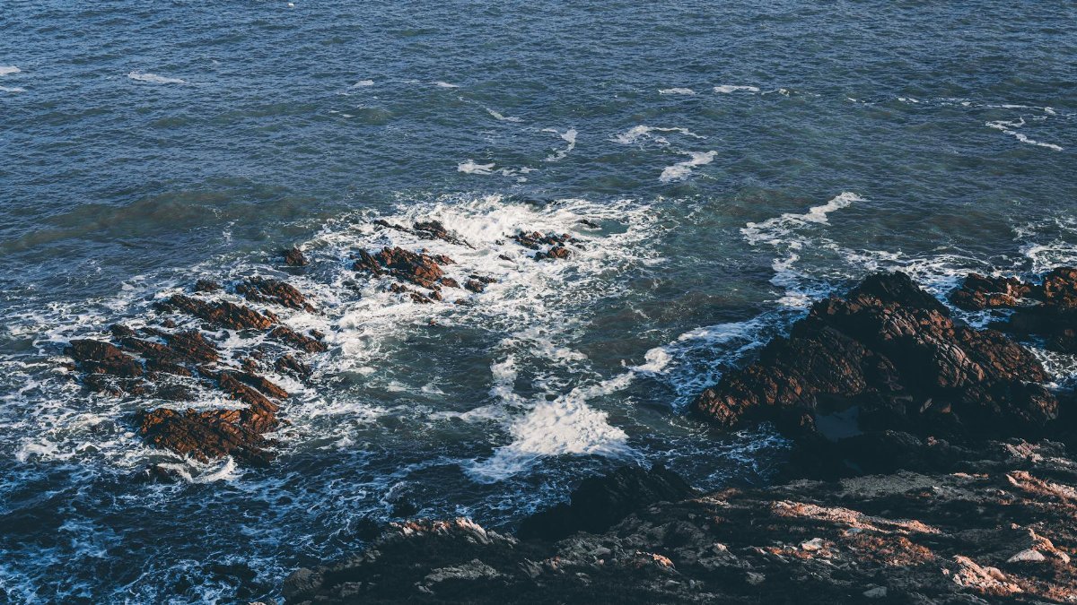 Scenic view of ocean waves crashing on rugged coastal rocks under natural light.