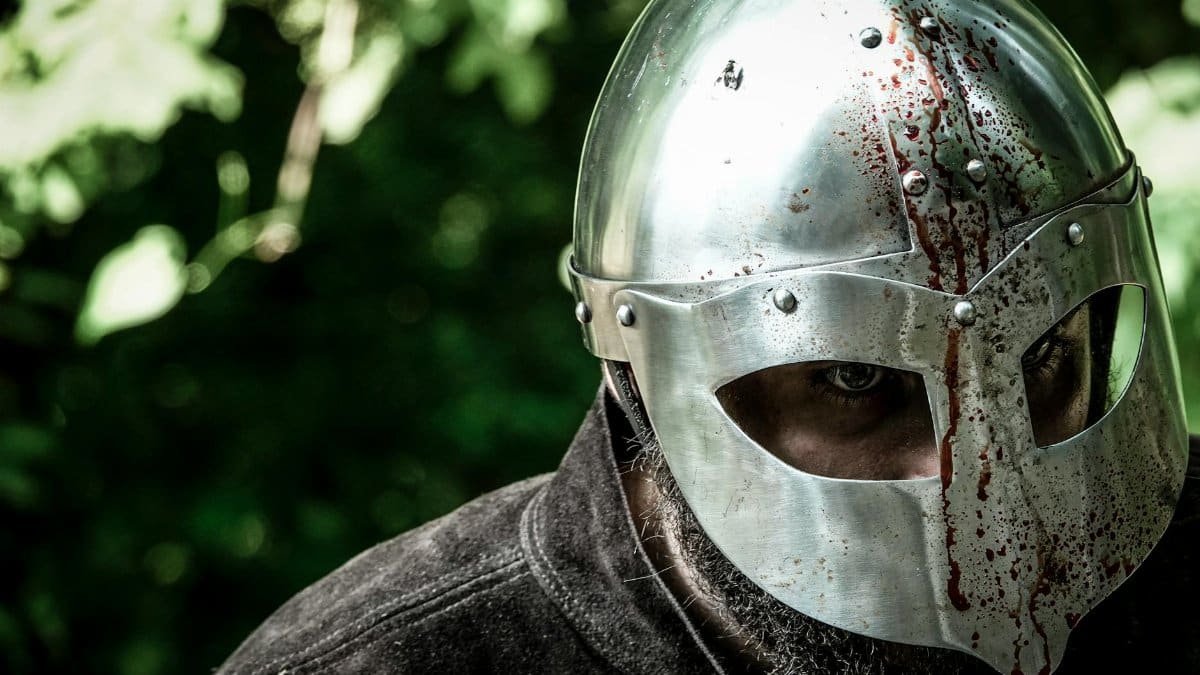 Close-up of a knight in a blood-stained helmet, evoking medieval combat.