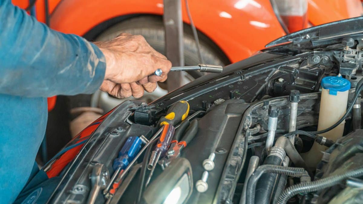 Mechanic performing maintenance on a car engine in a garage setting, using various tools.