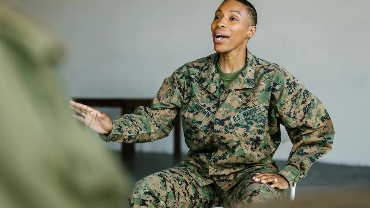 Female veteran in U.S. Marine Corps uniform smiling and gesturing during a discussion indoors.