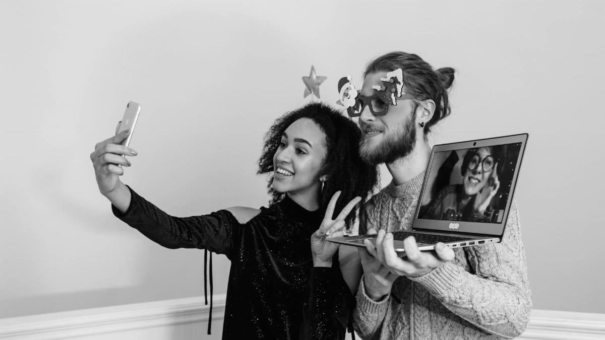 A couple taking a playful selfie with a laptop video call in black and white.