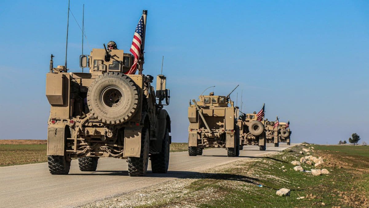 American military convoy driving through rural Syria under a blue sky.