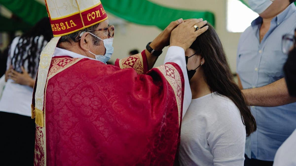 A bishop performs a confirmation on a teenager in a traditional religious ceremony.
