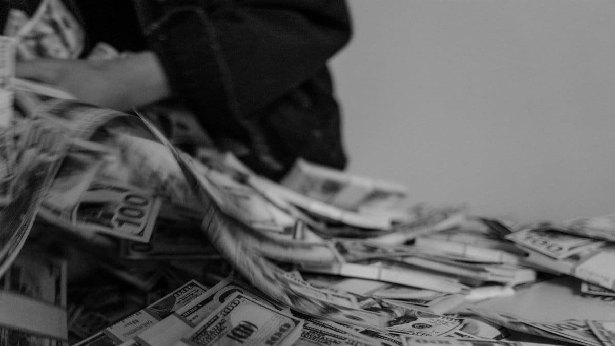 A blur of hands moving through a pile of US dollar bills, captured in black and white.