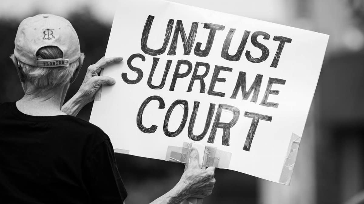 Black and white photo of a protester holding a sign saying 'Unjust Supreme Court' during a demonstration.