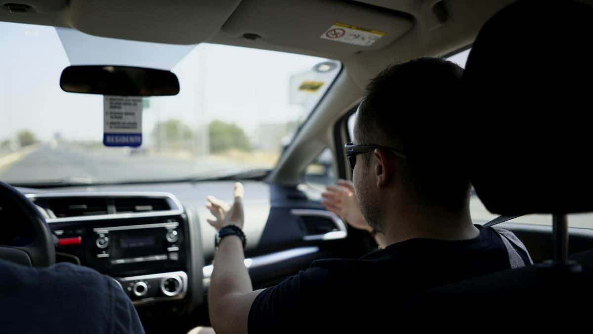Passenger gesturing while conversing during a car journey on a sunny day.