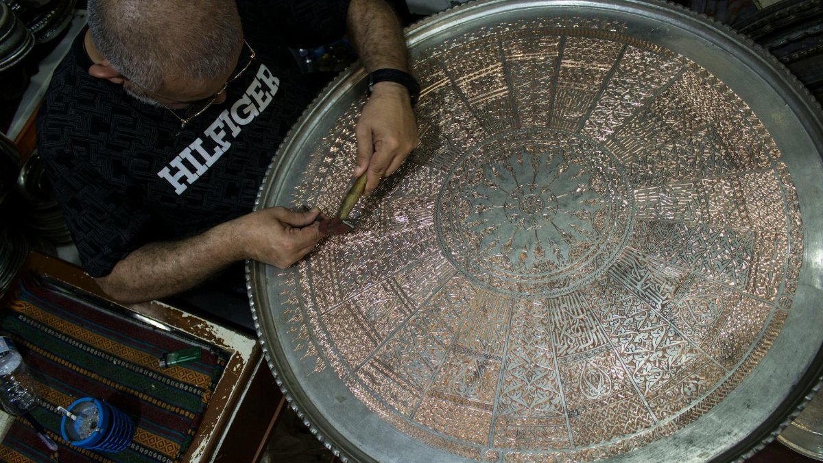 Skilled craftsman engraving intricate design on a large copper tray in Gaziantep, Türkiye