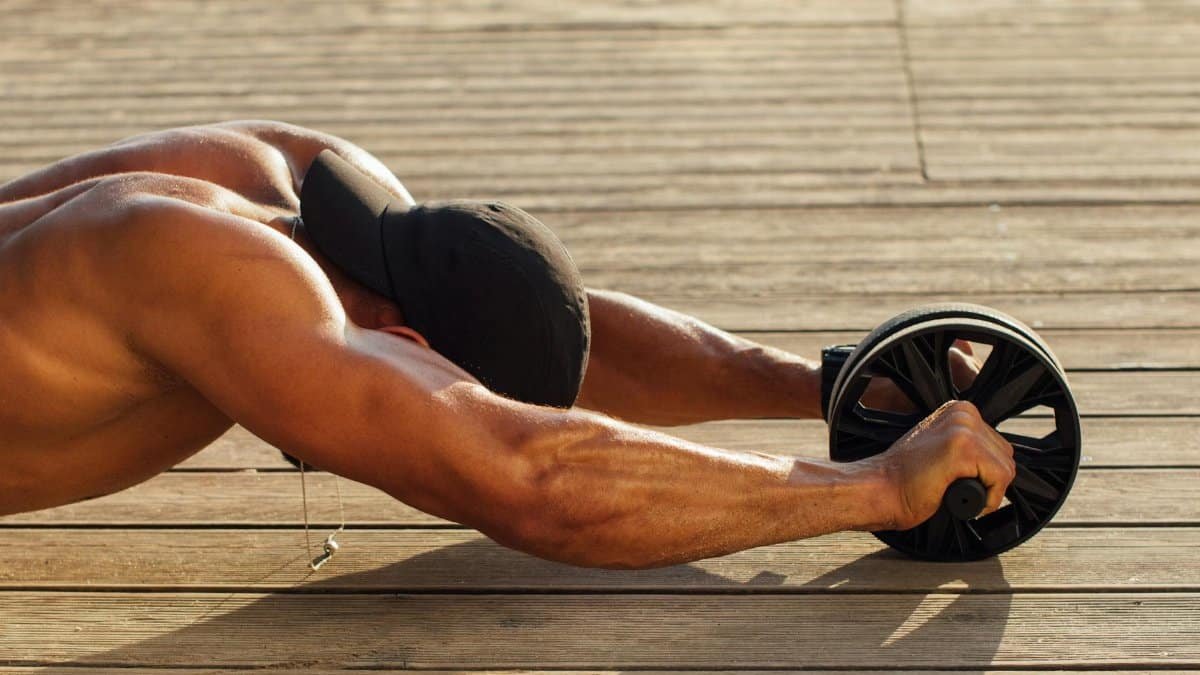 Strong man using an ab roller on wooden deck for core strength and fitness outdoors.