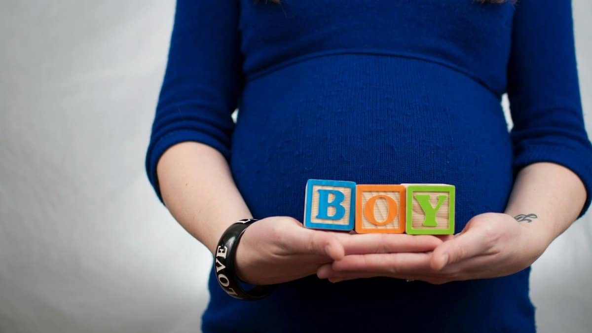 Pregnant woman in blue dress holds 'boy' blocks, symbolizing a baby boy announcement.