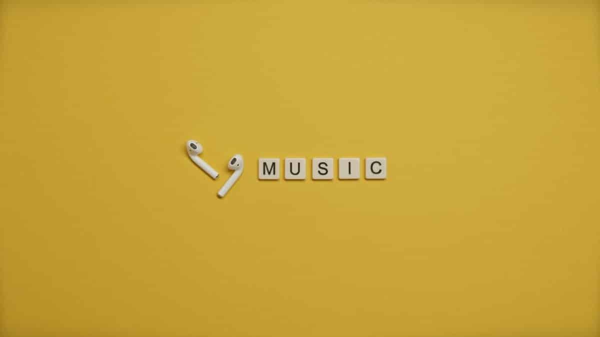 Minimalist image of AirPods and music-themed letter tiles on a vibrant yellow background.