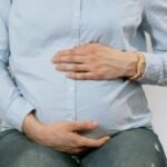 Pregnant woman sitting indoors, hands on belly, wearing casual clothes. Healthcare consultation setting.