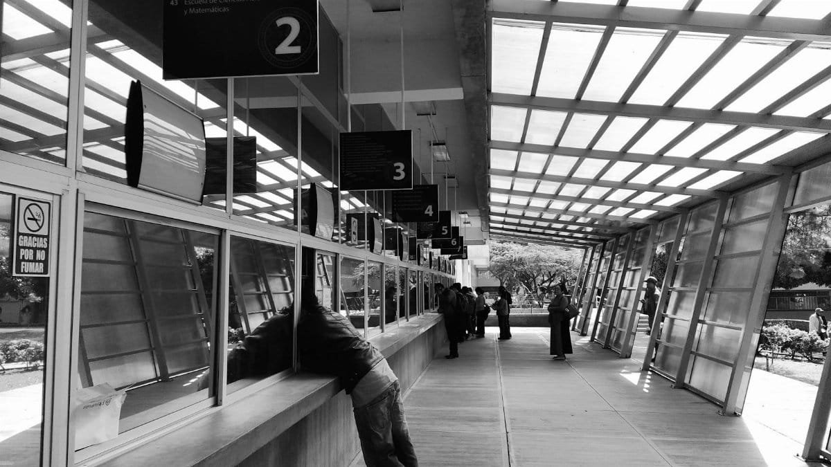 People queuing indoors at a service counter in Ciudad de Guatemala captured in black and white.