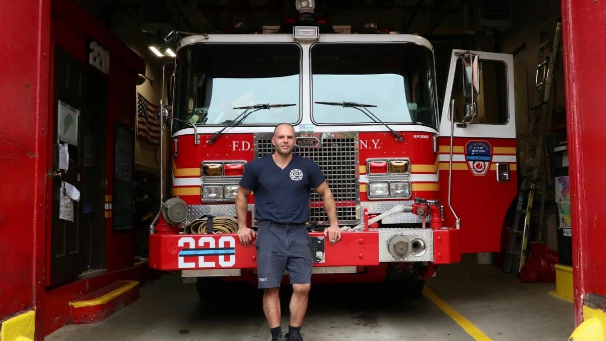 A firefighter stands in front of an FDNY fire truck in a New York City fire station.