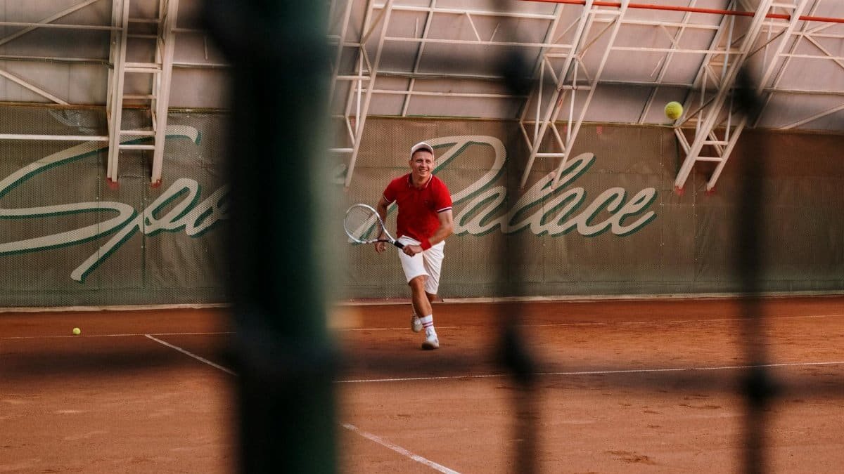 A male tennis player in action on a clay court at Sports Palace indoor facility.