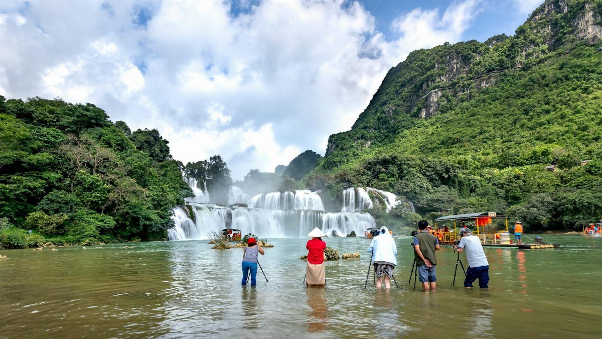 Visitors photographing the beautiful Ban Gioc Waterfall surrounded by lush greenery in Vietnam.