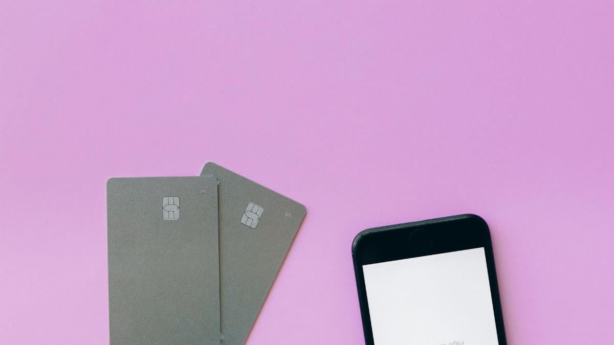 Flat lay of credit cards and smartphone on pink surface, symbolizing digital payment solutions.