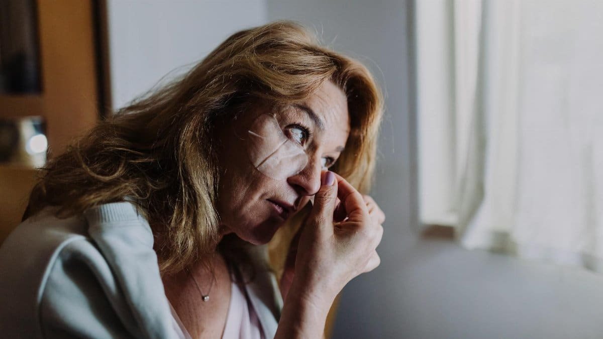 A woman applies an eye patch symbolizing self-care and relaxation indoors.