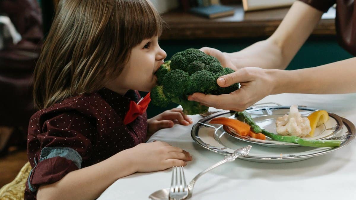Cute child eating broccoli, promoting healthy eating habits indoors.