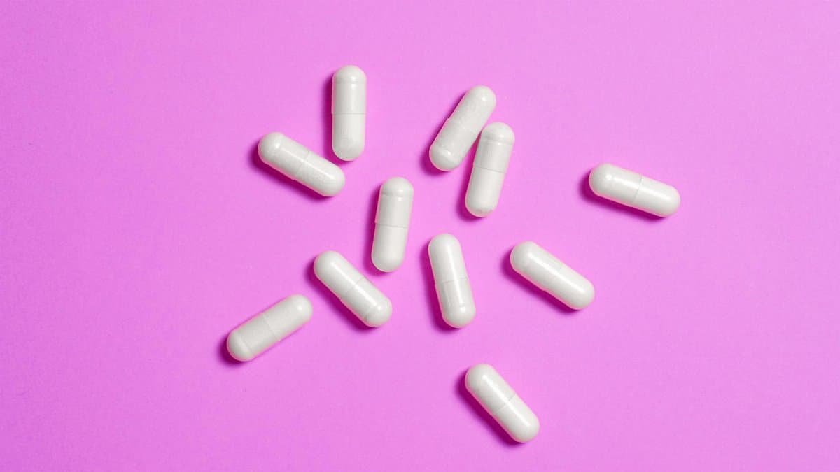 White medicine capsules scattered on vibrant pink background, highlighting modern pharmaceutical design.