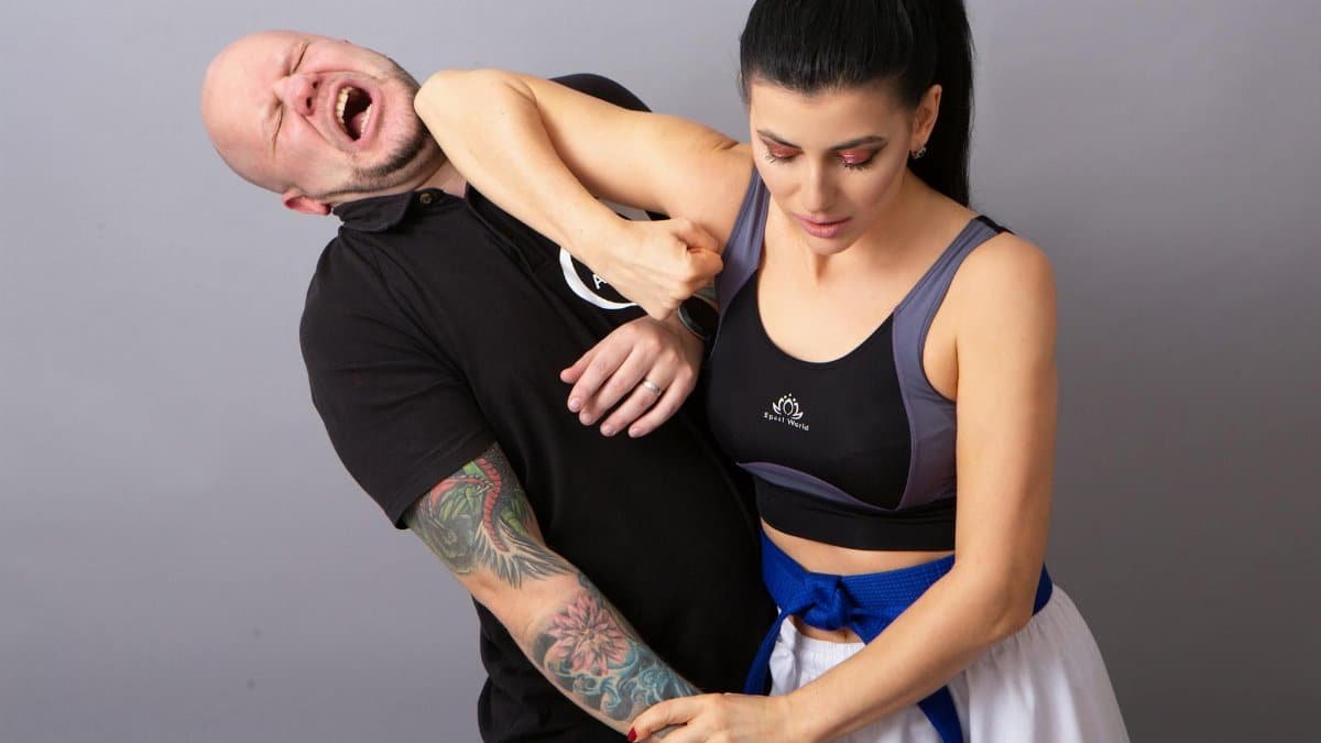 Woman in sports bra demonstrating self-defense martial arts against a man indoors.