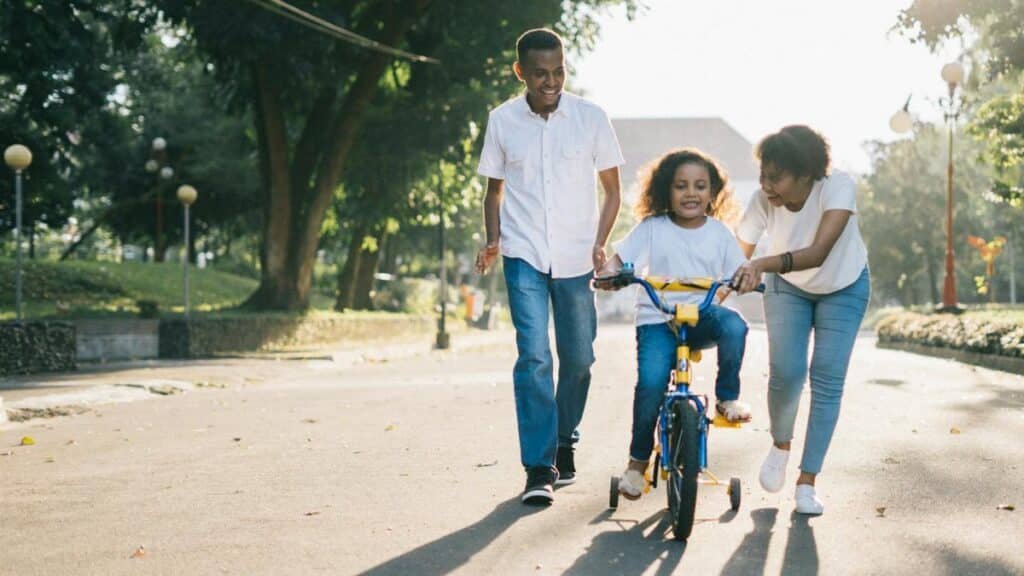 Happy family teaching their child to cycle on a sunny day outdoors.