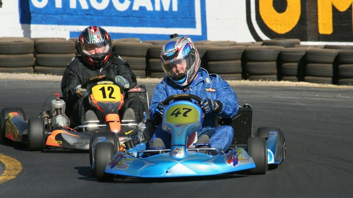 Two racers navigate a sharp turn in a competitive go-kart race on an outdoor circuit.