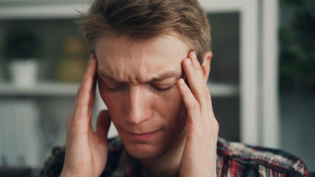 Man experiencing stress or headache, closing eyes and rubbing temples indoors.
