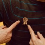 A man proudly highlighting his 'Best Dad Ever' badge on a striped sweater against a yellow background.