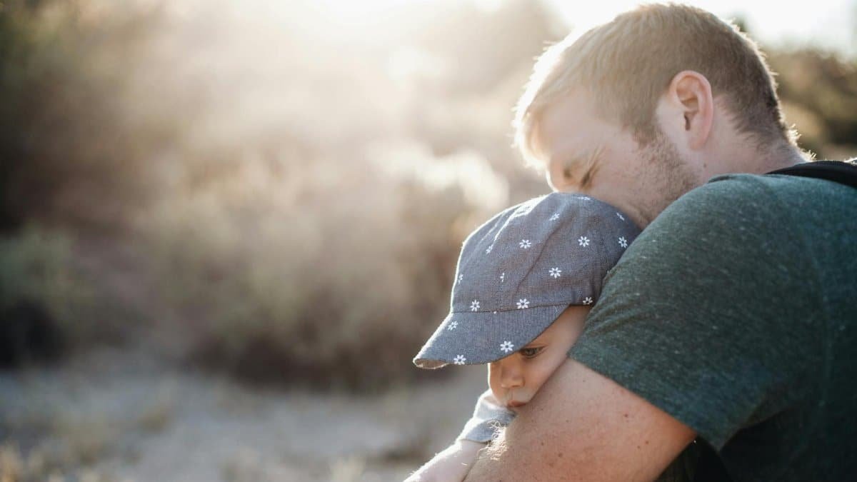 A father lovingly embraces his baby outdoors on a sunny day. Perfect for Father's Day themes.