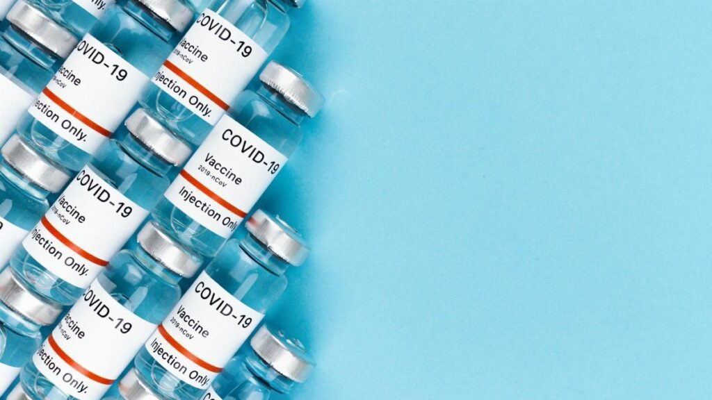 Array of COVID-19 vaccine vials on a blue surface, offering ample copy space.
